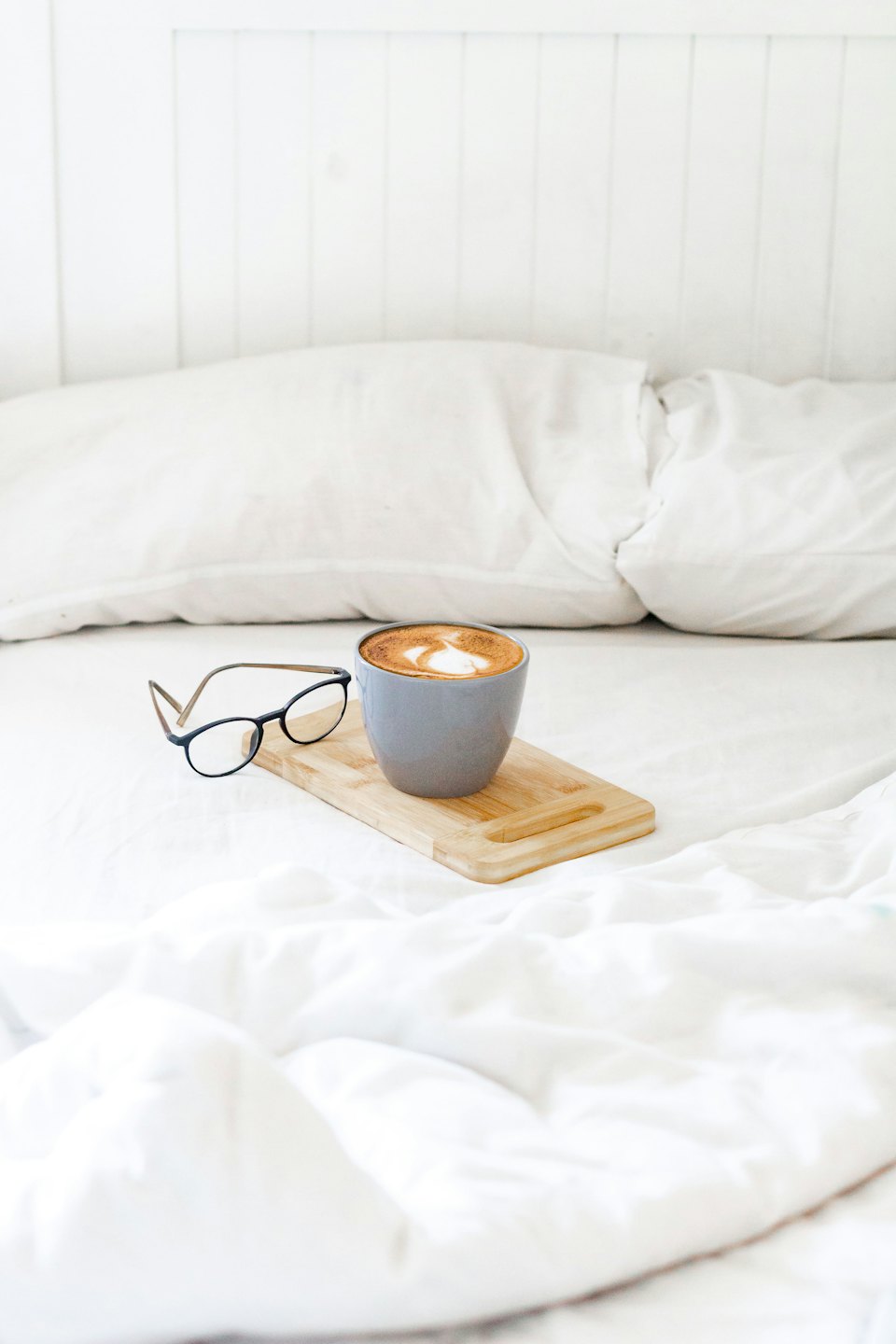 A cup of coffee and glasses rest on a wooden tray.