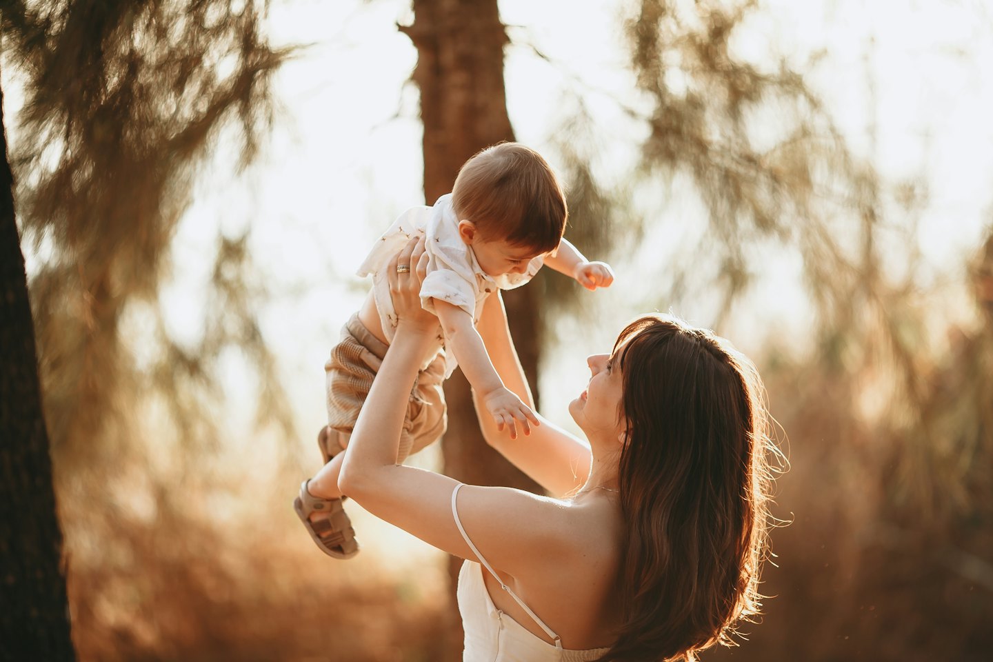 Mother playfully lifts her baby into the air outdoors.