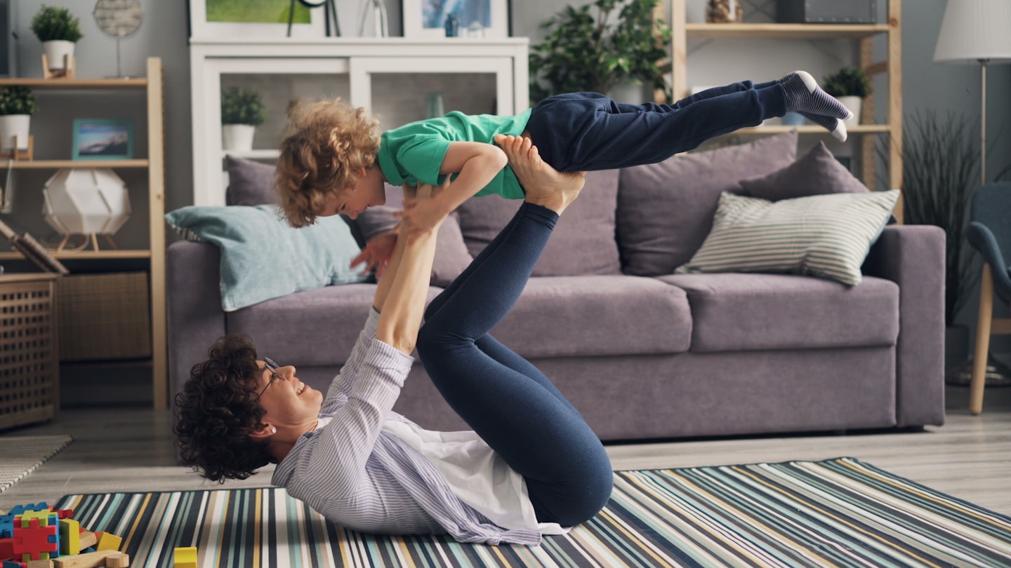 A woman lifts a smiling child into the air while lying on a rug.